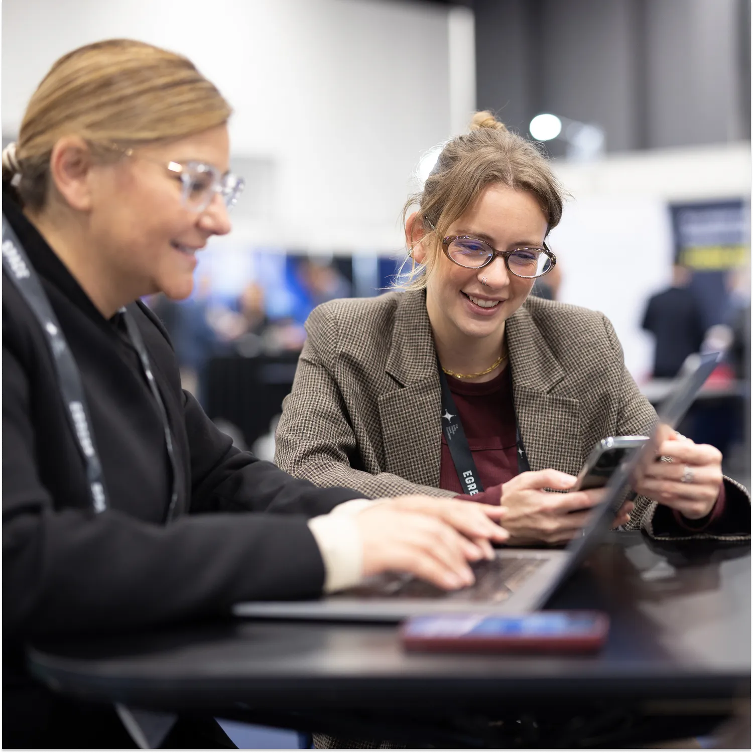 Two delegates smiling at a laptop and phone at the Australian Space Forum